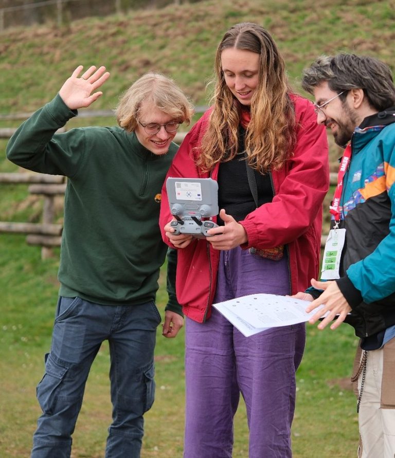 Drei Personen mit Controllern hören einem Trainer zu, während ein Drohne fliegt.
