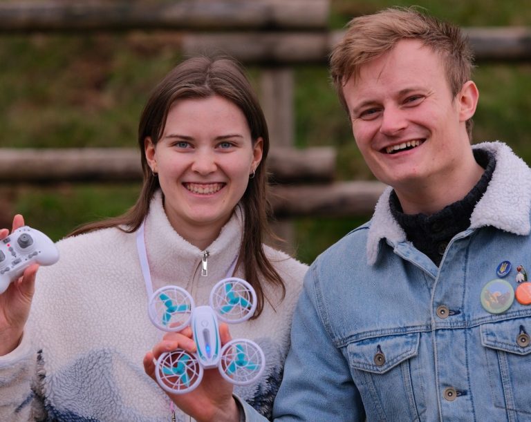Zwei junge Personen lächeln und halten jeweils ein Spielzeug in der Hand.